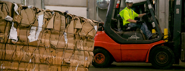 A bundle of recycled cardboard with a forklift in the background.